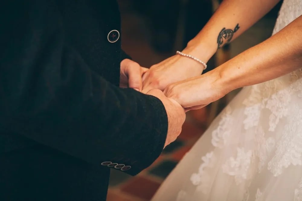 Bride's wrist with a small black arrow tattoo, holding hands with the groom