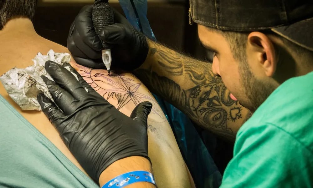 Tattooer in black gloves working over a stencil on a client's back