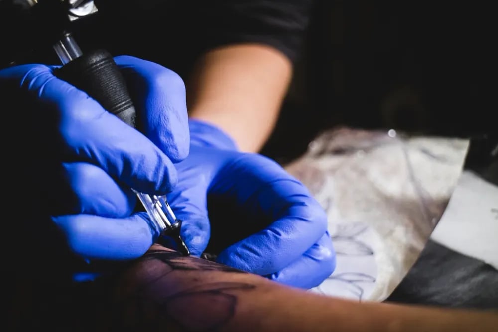 Artist in blue gloves working on a forearm