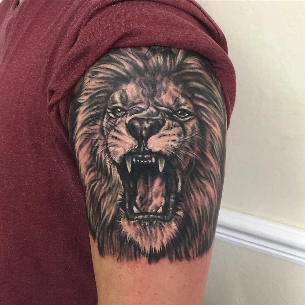 Black and grey realistic roaring lion tattoo on an upper arm