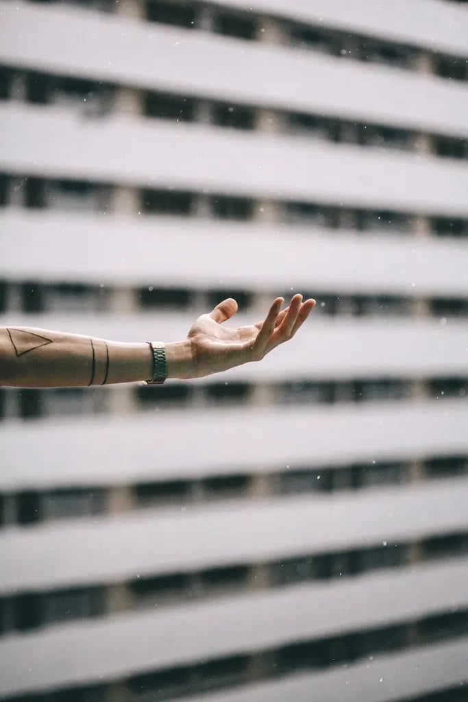 Outstretched arm with a minimal geometric tattoo in front of a building