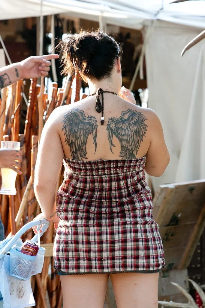 Black and grey feathered wings tattooed across a woman's upper back
