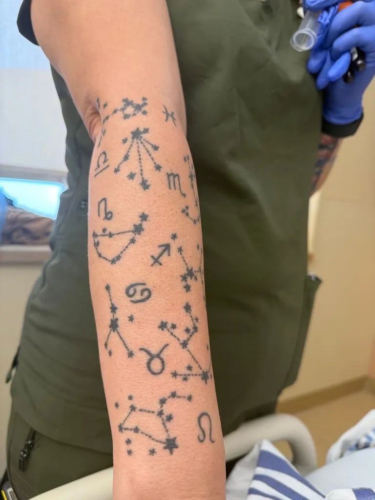 Forearm covered in small fine line zodiac constellations and their signs
