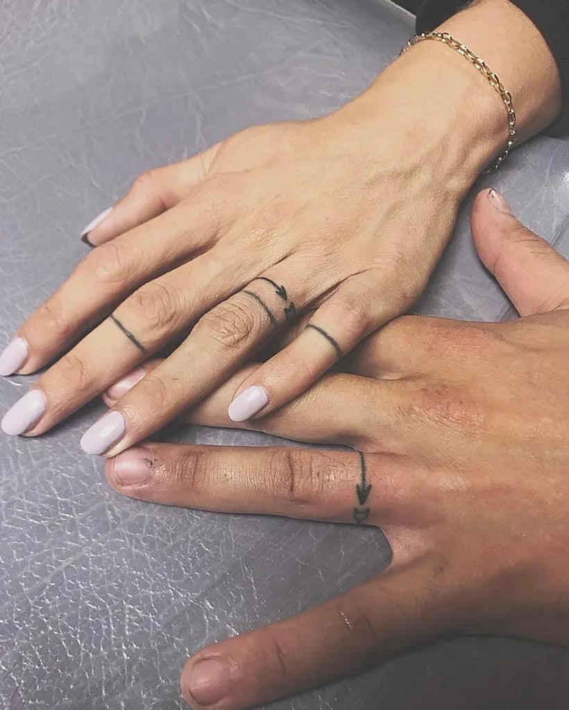 Two hands resting together, each with thin ring tattoos on the fingers