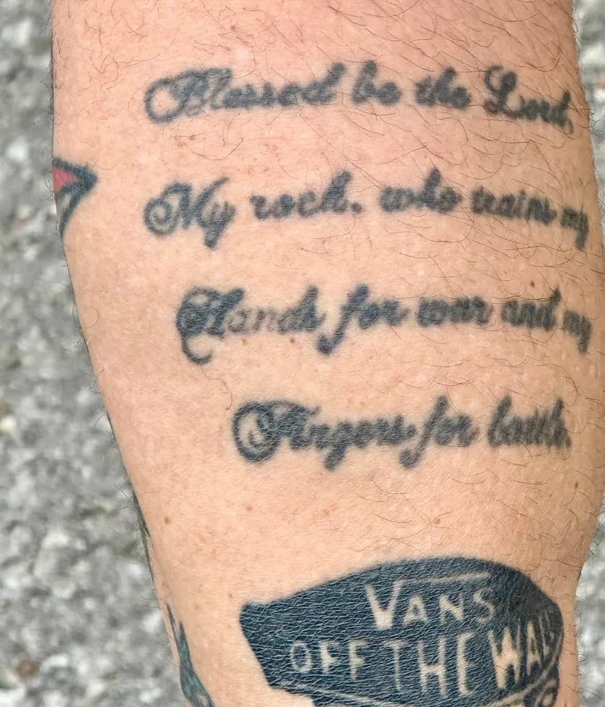 Calf tattoo of a psalm in black script above a small shoe-brand logo
