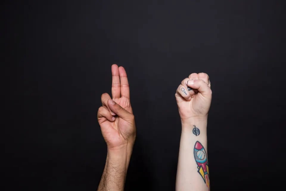 Two raised hands with small matching wrist tattoos